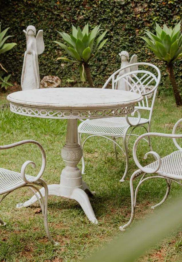 Mesa e cadeiras de ferro branco no jardim da pousada