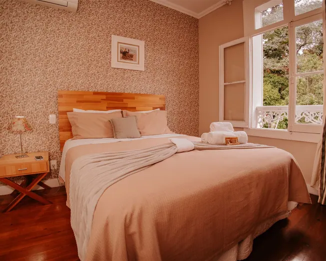 Quarto duplo com cama de casal, cabeceira de madeira e janela para o jardim